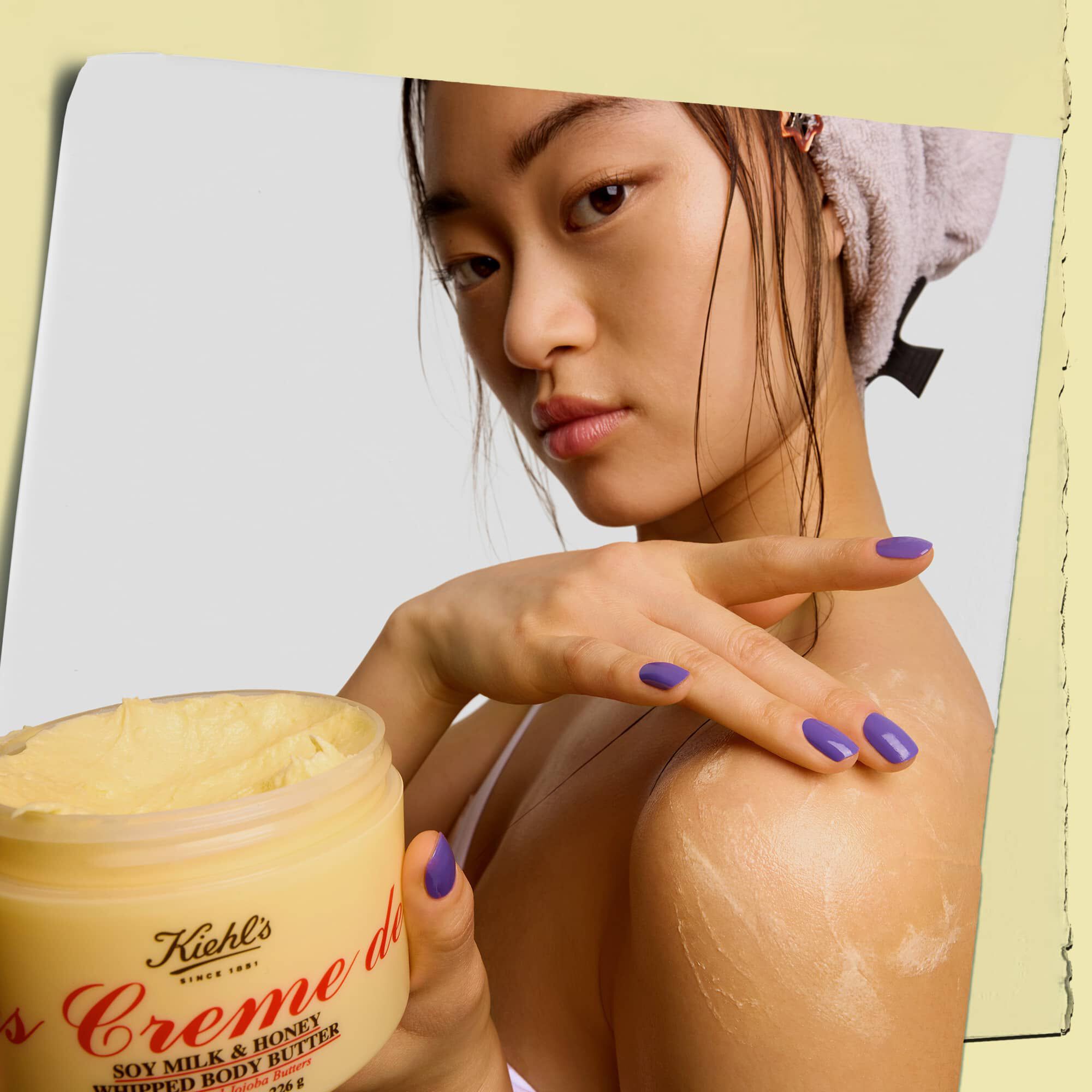 Modelo sosteniendo un tarro y aplicandose la manteca corporal Kiehl's Creme de Corps Whipped Butter