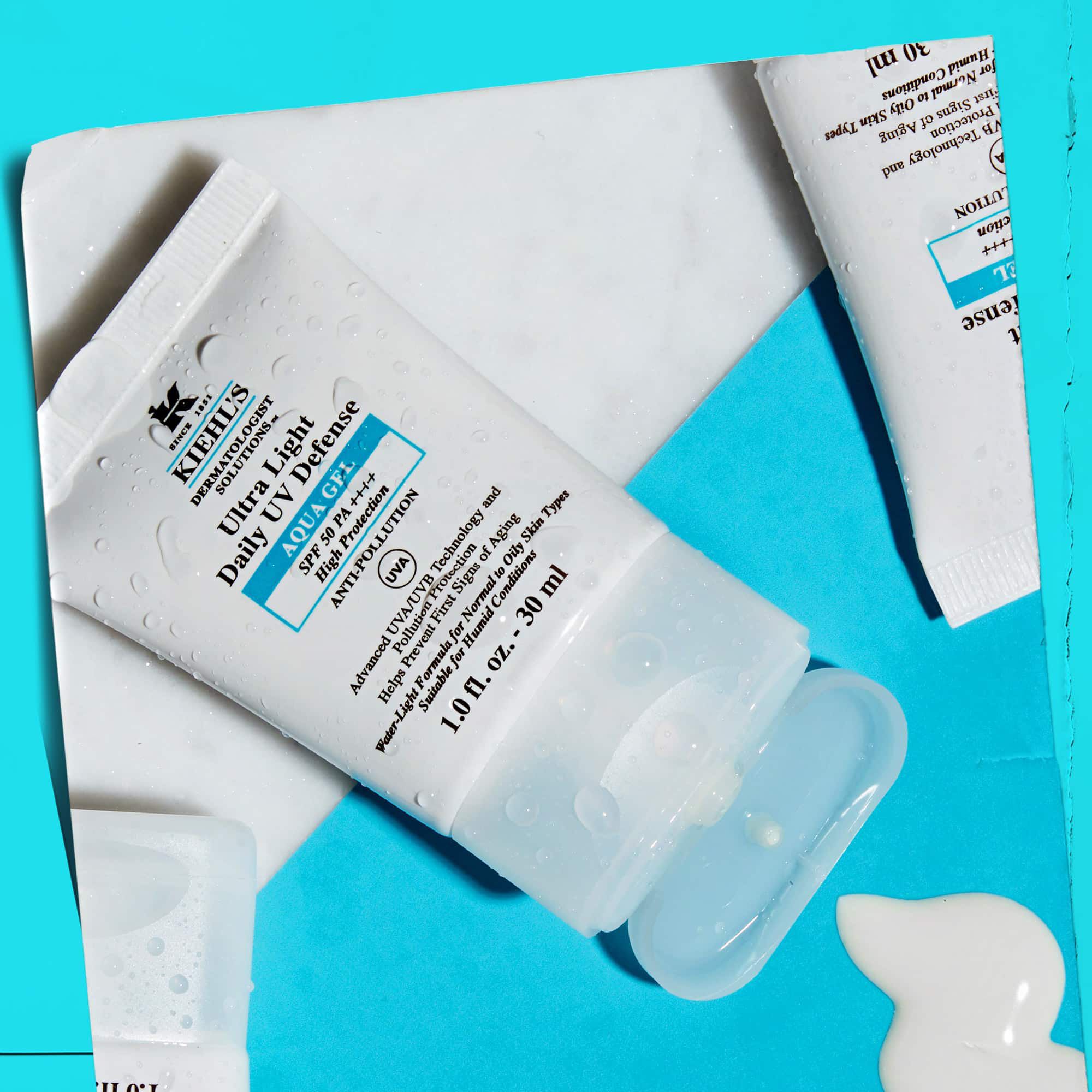 Una composicion plana de varios tubos de Ultra Light Daily UV Defense Aqua Gel sobre una superficie de marmol, mostrando su atractivo estilo de vida.