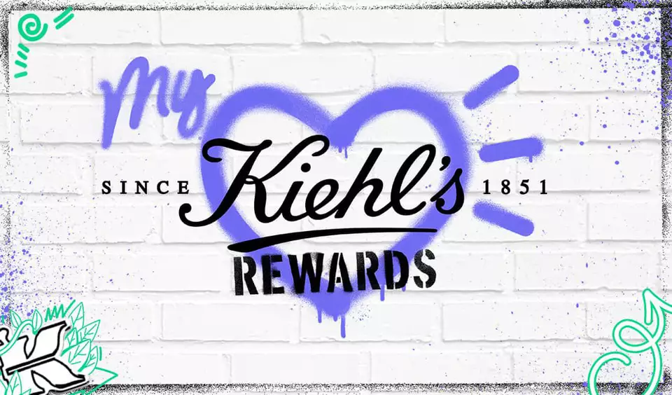 Texto alternativo: "Fondo de ladrillo blanco con el logo de Kiehl's en el centro, presentado dentro de un corazon morado, acompanado de elementos graficos coloridos con la palabra 'REWARDS'."