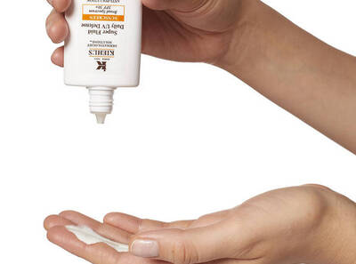 Una mano vierte crema hidratante Kiehl's sobre la otra, mostrando el uso del producto para el cuidado diario de la piel.