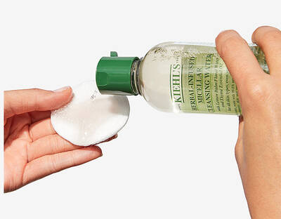 Botella de limpiador facial Kiehl's vertiendo producto sobre un disco de algodon en manos.