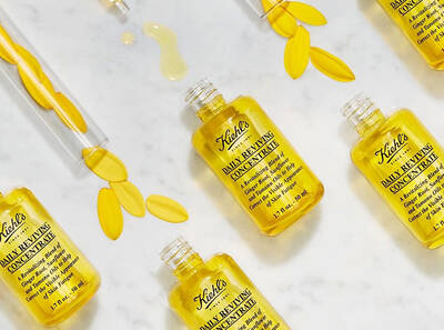 Botellas de aceite concentrado de Kiehl's sobre un fondo blanco, rodeadas de petalos amarillos y gotas de producto.