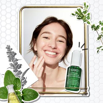 Mujer sonriente aplicando serum de aceite de cannabis de Kiehl's frente a un espejo. Elementos botanicos alrededor.