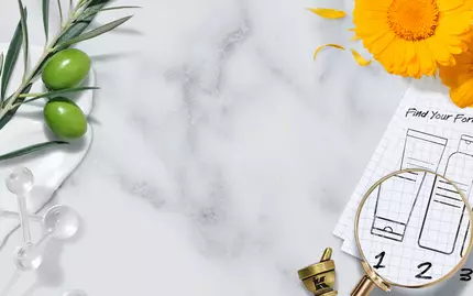 A flat lay featuring a marble background with various natural ingredients, including olive branches and herbal elements, alongside a magnifying glass and a blueprint of product formulas. A blank white area in the center is framed by an elegant border.
