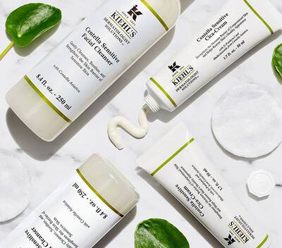 Productos de Kiehl's: limpiador facial y crema, sobre una superficie de marmol con discos de algodon y hojas decorativas.