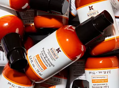 A collection of Kiehl's orange bottle skincare products stacked together, featuring labels and black pumps.