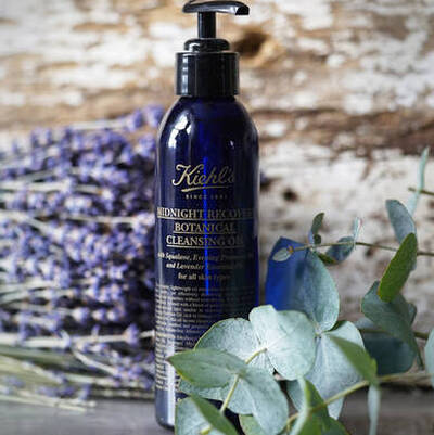 Botella de aceite limpiador de Kiehl's con lavanda, rodeada de ramas de eucalipto y flores secas.