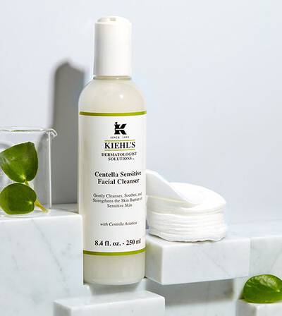 Botella de limpiador facial 'Centella Sensitive' de Kiehl's, sobre una superficie de marmol con discos de algodon al fondo.