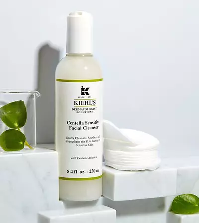 Botella de limpiador facial 'Centella Sensitive' de Kiehl's, sobre una superficie de marmol con discos de algodon al fondo.