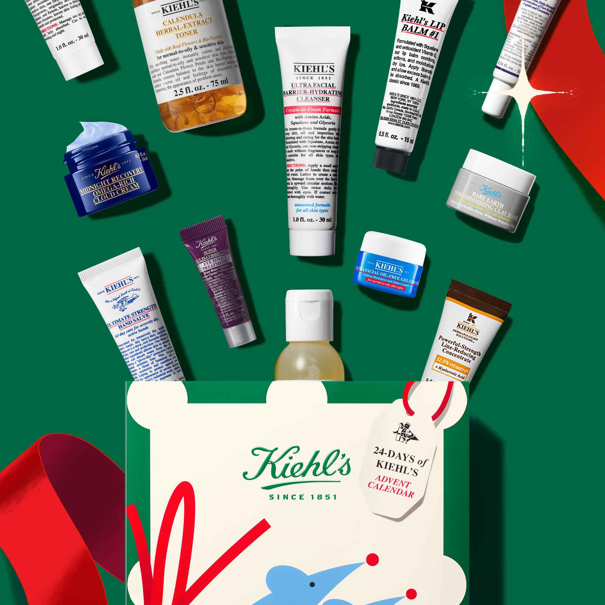 Hands hold a Kiehl’s holiday gift box with colorful abstract design, logo, and “Since 1851” tag on a festive green background.​