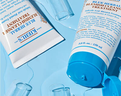 Productos de cuidado facial de Kiehl's sobre un fondo azul, incluyendo tratamientos para imperfecciones y limpieza.
