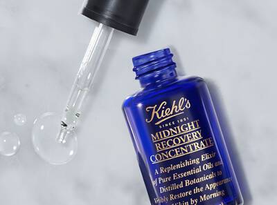 Botella de suero Kiehl's Midnight Recovery Concentrate, con un gotero y unas gotas de aceite en la superficie.