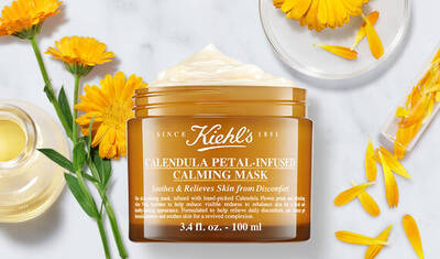 Tarro de mascarilla calmante de Kiehl's, infundida con petalos de calendula, rodeado de flores y aceite.