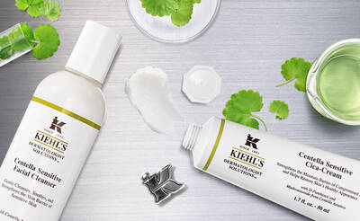 A flat lay image featuring Kiehl's Centella Sensitive Facial Cleanser and Centella Sensitive Cica-Cream, surrounded by green leaves and a small glass of water on a metallic surface.