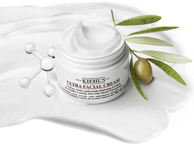 Crema hidratante facial Kiehl's Ultra Facial en un fondo blanco con aceite y oliva, destacando su textura suave.