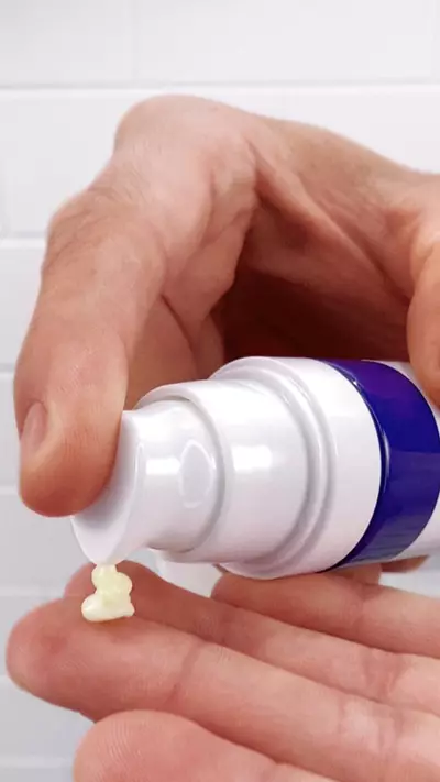 Mano sosteniendo un envase de crema, con una pequena cantidad de producto goteando sobre la palma.