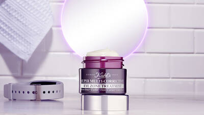 Crema para la zona de los ojos de Kiehl's, con envase elegante, sobre una superficie blanca junto a un reloj.