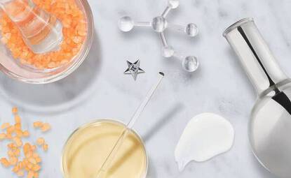 Texto alternativo: Variedad de productos de cuidado de la piel sobre una superficie blanca, incluyendo frascos y gotas de suero.