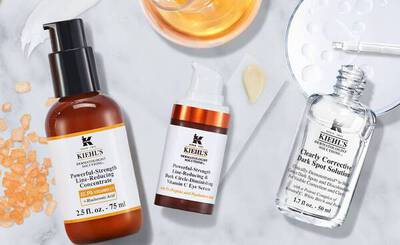 Productos de Kiehl's: sueros para reducir lineas y manchas oscuras, sobre un fondo de marmol con gotas y especias.