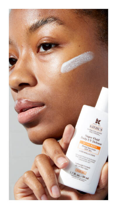 Una mujer aplica protector solar Kiehl's en su rostro, mostrando la textura del producto en su piel morena.