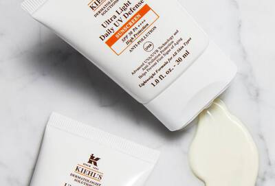 Crema solar Kiehl's Ultra Light Daily Defense, tubos abiertos con producto derramado, fondo blanco.