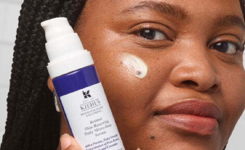 Primer plano de una mujer con trenzas, sosteniendo un suero
                                        Kiehl's Retinol
                                        Daily Micro-Dose, con una gota del producto aplicada en su mejilla.