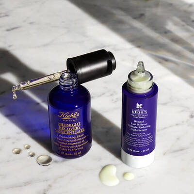 Frascos de sueros de Kiehl's sobre una superficie de marmol, uno con cuentagotas y otro con tapon de rosca.