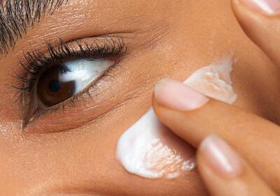 Una persona aplica crema facial en su piel, centrando la atencion en su ojo y la textura del producto.