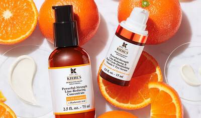 Frascos de serum Kiehl's sobre fondo de naranjas, destacando productos anti-edad con vitamina C y acido hialuronico.