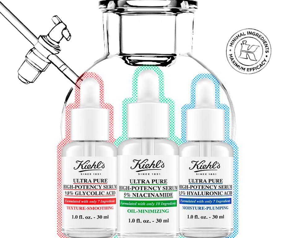Tres frascos de sueros para el cuidado de la piel de Kiehl's, etiquetados en colores rojo, verde y azul, acompanados de un gotero sobre un fondo blanco.