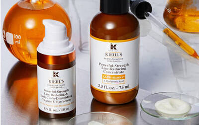 Frascos de productos de belleza de Kiehl's, incluyendo suero y concentrado, sobre fondo de mesa con utensilios de laboratorio.