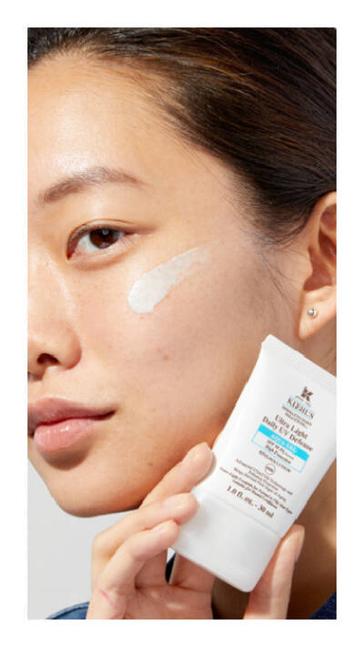 Mujer aplicando crema facial con un dedo, sosteniendo un tubo de Kiehl's Daily Reviving Concentrate.